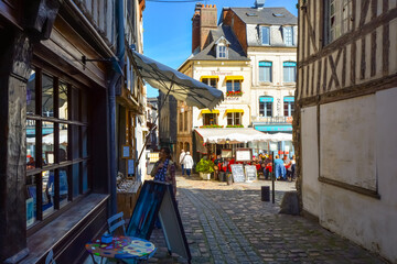 Fototapeta na wymiar A woman window shops on a sunny day in the Normandy town of Honfleur France with an outdoor sidewalk cafe behind her