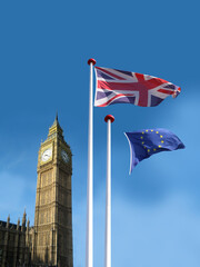 Fototapeta na wymiar Flagpoles in front of Big Ben clocktower in London with flag og the United Kingdom waving and the European Union flag leaving the flagpoleand blowing away. UK leaving EU concept. Blue sky background.