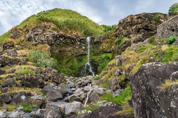 Rocks and grass with mount and waterfall on cliff from Viola beach, São Miguel - Azores PORTUGAL