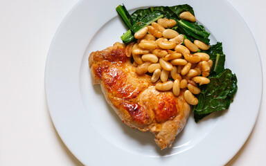Pan-seared pork with white beans, kale, and garlic served on a white plate. Homemade nutritional protein-rich healthy food.
