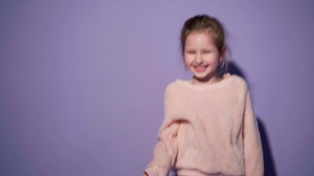 little girl, a child laughing on a purple background in the studio. A cute positive child in a fluffy sweater is happy and laughs merrily.