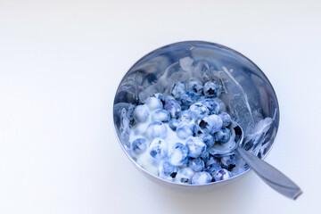 Fresh organic blueberries mixed with yogurt in a blue bowl on white background