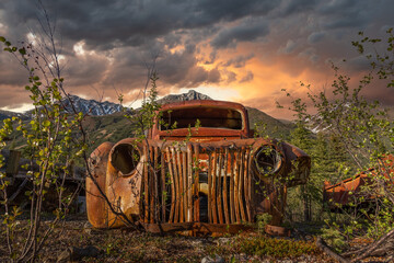 Fototapeta na wymiar Abandoned 1940s style rusty truck that sits in the Yukon Territory wilderness in northern Canada. Seen in the summer time with midnight sun and stormy clouds building behind. 