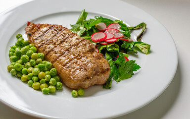 Homemade pork steak with cilantro, scallion, green peas, and sliced red radish, view from diagonally above close-up