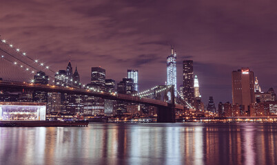 Naklejka na ściany i meble Illuminated Brooklyn Bridge And Buildings By River Against Sky At Night in New York City