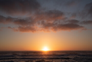 A ocean, sea sunset in northern California during spring time with sun shining over the horizon and tide below. 