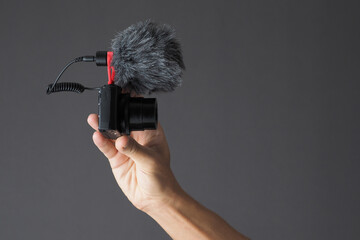 Male hand holding compact camera with microphone on gray background. Vlog concept.