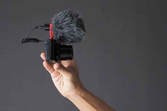 Male hand holding compact camera with microphone on gray background. Vlog concept.