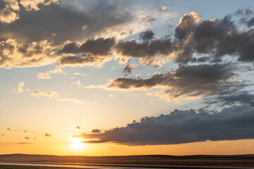 Sunset theme for sky replacement background with dark themed clouds, blue sky and sun shining on the horizon. Great for tranquil, calm, serene country or rural themed art.