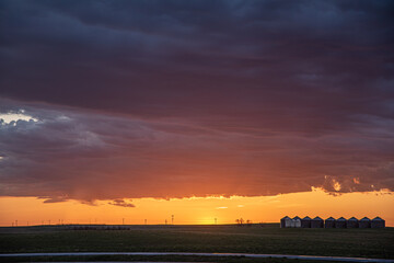 A flat landscape seen before a cloudy storm approaching with pink dark clouds, shining sun and dark country, rural land below. Great for sky replacement for editing photos or drawing. 