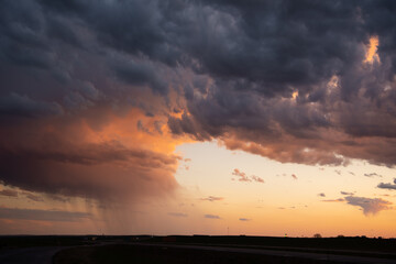 A flat landscape seen before a cloudy storm approaching with pink, orange dark clouds, shining sun and dark country, rural land below. Great for sky replacement for editing photos or drawing. 