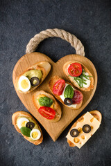 Fototapeta na wymiar Open faced sandwich canape or crostini on a wooden serving board on dark stone background closeup. Top view.