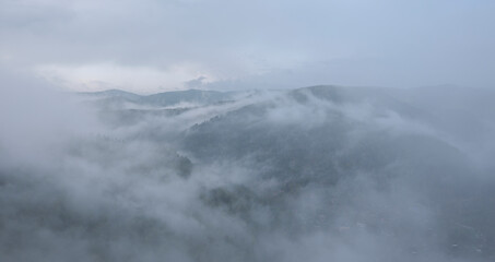 Naklejka premium Fog in the mountains. Green forest in the highlands, residential buildings in the valley.