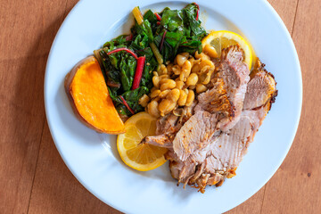 Pork roast with chard, bean, and squash on a white plate