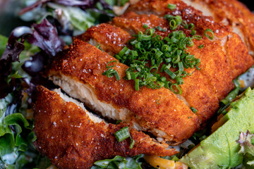 Breaded chicken breast with chives on a bed of greens