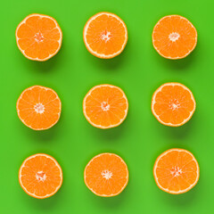 Fruit pattern of fresh orange slices on green background. Flat lay, top view. Pop art design, creative summer concept. Half of citrus in minimal style.
