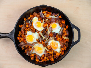 Sweet Potato Hash with Baked Eggs Paleo Diet Meal in Black Cast Iron Pan on Plain Maple Wood Table