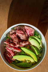 Avocado and grilled steak bowl on maple wood backgrounds with upward shadows