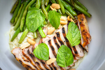Sliced grilled chicken and string bean with peanuts and mint leave on a noodle in a white bowl. Top view.