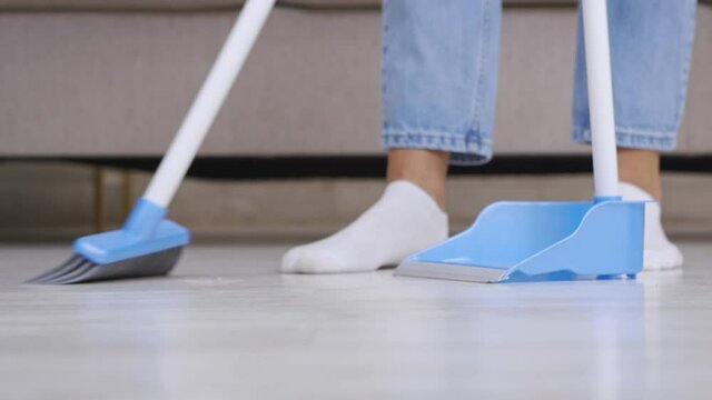 Domestic routine. Close up of woman sweeping floor at home with broom and scoop, slow motion