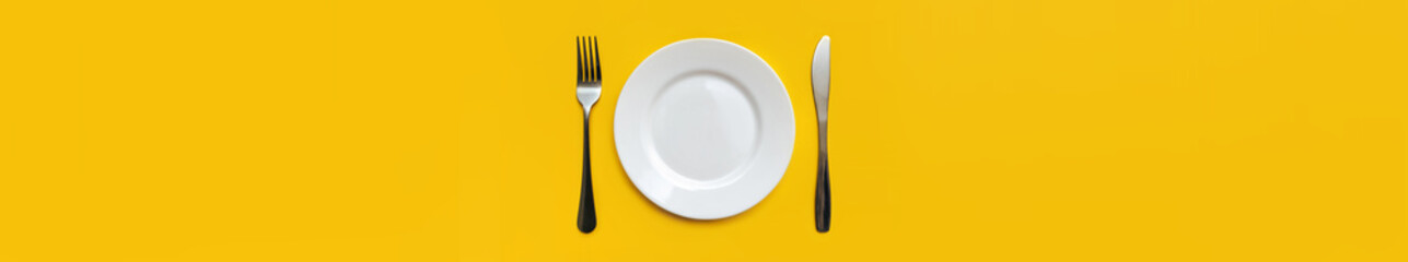 White plate and stainless fork and knife lie on a yellow tablecloth. The concept of minimalist table setting, top view. Copy space, mockup.