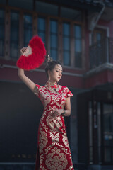Beautiful Asian woman, model,  wearing traditional red cheongsam qipao dress holding red foldable feather fan in China Town for Chinese new year concept.