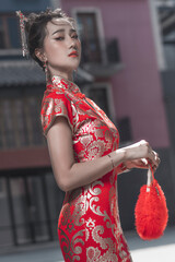 Beautiful Asian woman, model,  wearing traditional red cheongsam qipao dress holding red foldable feather fan in China Town for Chinese new year concept.