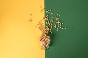 Soyabeans pouring splashing from hart shape glass bottle on yellow green background