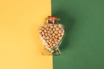 hart shape glass bottle filled with soya beans on yellow background