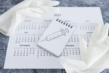 covid-19 vaccine against the pandemic, 2021 calendar with syringe sketch on notepad and disposable gloves on it