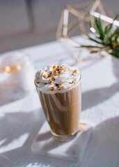 Coffee glass on top of a coaster  topped with whipped cream and cone sugar and a plant in the background
