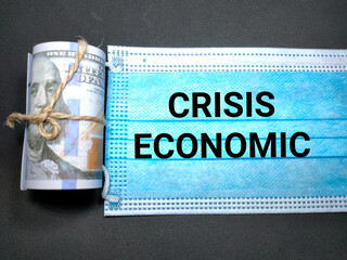 Obraz premium Selective focus of a banknote and text CRISIS ECONOMIC on a face mask with gray background.Shot were noise and grain.
