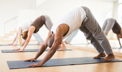 Fototapeta na wymiar Portrait of focused man making yoga exercises with friends at fitness center
