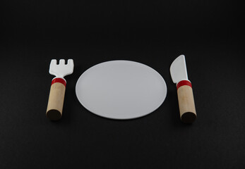Wooden knife and fork and white plate, food icon. Black background and copy space