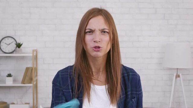 Close up portrait of angry furious tired woman shouting at camera and waving rag, reproaching for mess at home
