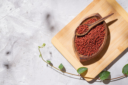 achiote grains in wooden bowl on white background (Bixa orellana)