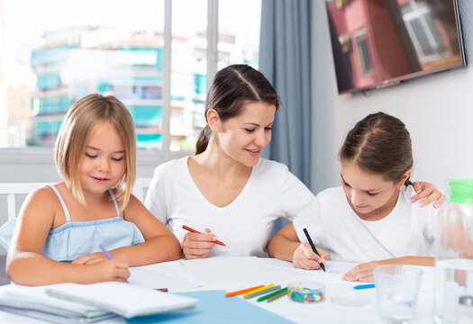 Woman with two kids drawing together sitting at table in living room