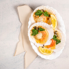 Baked scallops with caviar and creamy garlic sauce in white plate. Scallops with lemon on white background with napkin. Top view. Copy space.