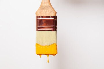 Close-up paintbrush with liquid yellow paint drips off the brush