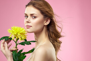 Beautiful girl with a yellow flower on a pink background nude shoulders makeup