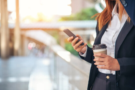 Businessman Businesswoman drinking coffee in town using smartphone outside office modern city. Hands holding take away coffee cup and smart phone talking together Business partner with cup of coffee