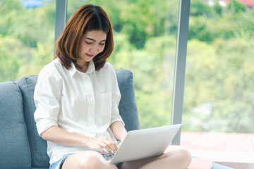 Woman working from home on laptop online meeting in home office. Entrepreneur asian business woman using notebook laptop sit on sofa technology new normal lifestyle. Happy woman typing keyboard laptop