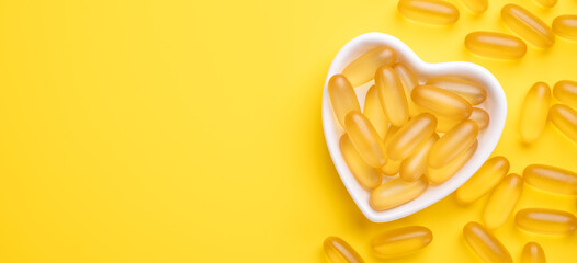 Omega 3 capsules in a heart-shaped plate on yellow background. Fish oil softgels. Supplement food vitamin D capsules. Copy space - Image - obrazy, fototapety, plakaty