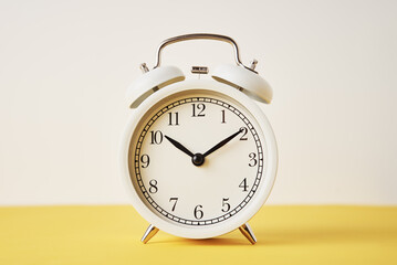 White vintage alarm clock on a yellow background with copy space