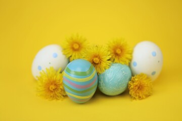 Easter holiday.Blue striped and white Easter eggs, yellow dandelion flowers on a bright yellow background.Spring religious holiday background. 