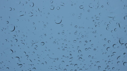 textured drops on transparent glass of a house or car window through which a heavy gloomy sky can be seen, abstract background of a rainy gray day, abstraction with water splashes