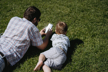 Father and son laying on grass watching something in smartphone