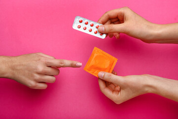 Female hands with wrapped condom and birth control pills on color background