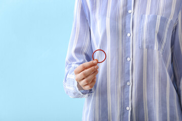 Woman holding contraceptive ring on color background