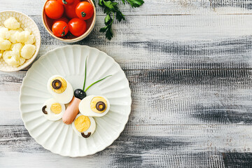 Creative breakfast for children with eggs, sausage and fresh vegetables on wooden background